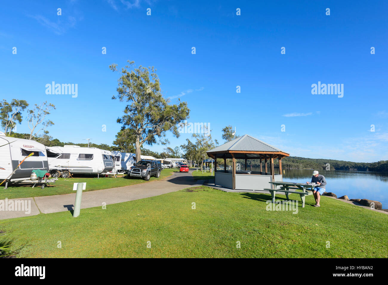 Uomo seduto in riva al lago sul lago di ingresso Conjola Holiday Park, Shoalhaven, South Coast, Nuovo Galles del Sud, NSW, Australia Foto Stock