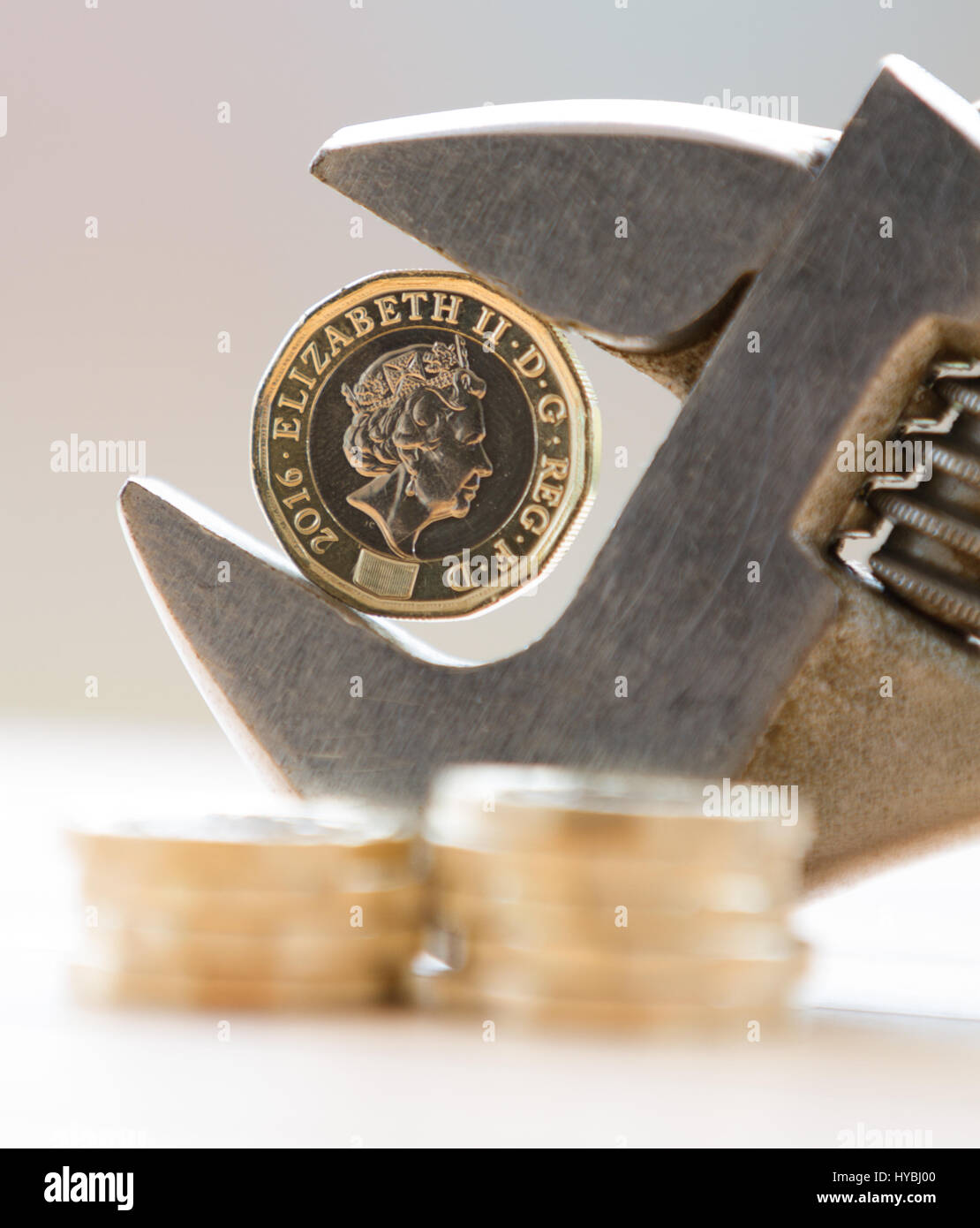 Nuovo una libbra di £ 1 moneta trattenuta in una chiave regolabile contro uno sfondo luminoso con monete impilate in primo piano che mostra un squeeze su finanze Foto Stock