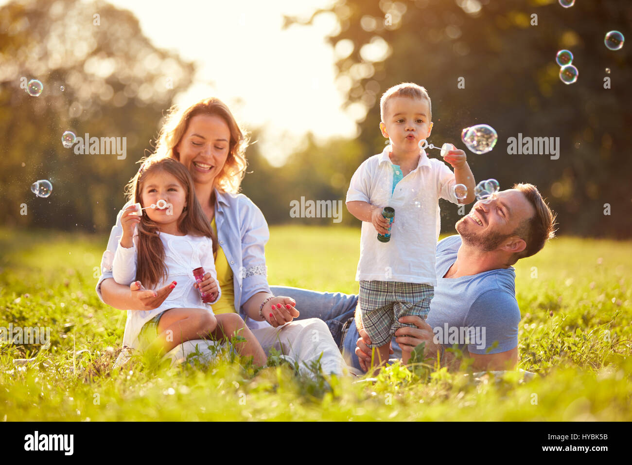 I genitori con bambini che si divertono in natura con bolle di sapone Foto Stock