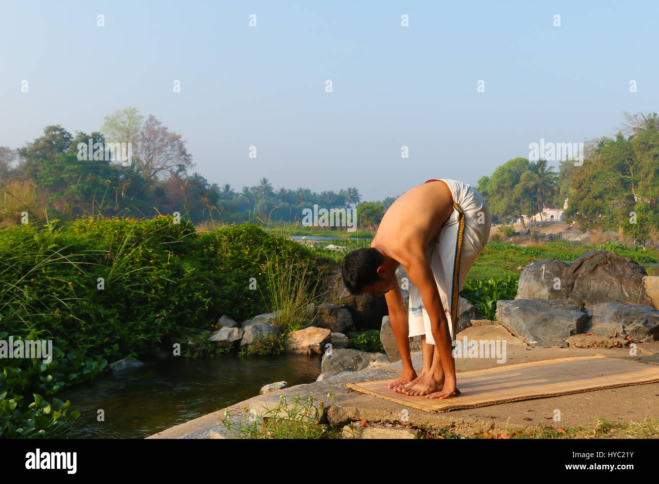 Uomo indiano a praticare yoga accanto a un fiume in India del Sud. Foto Stock