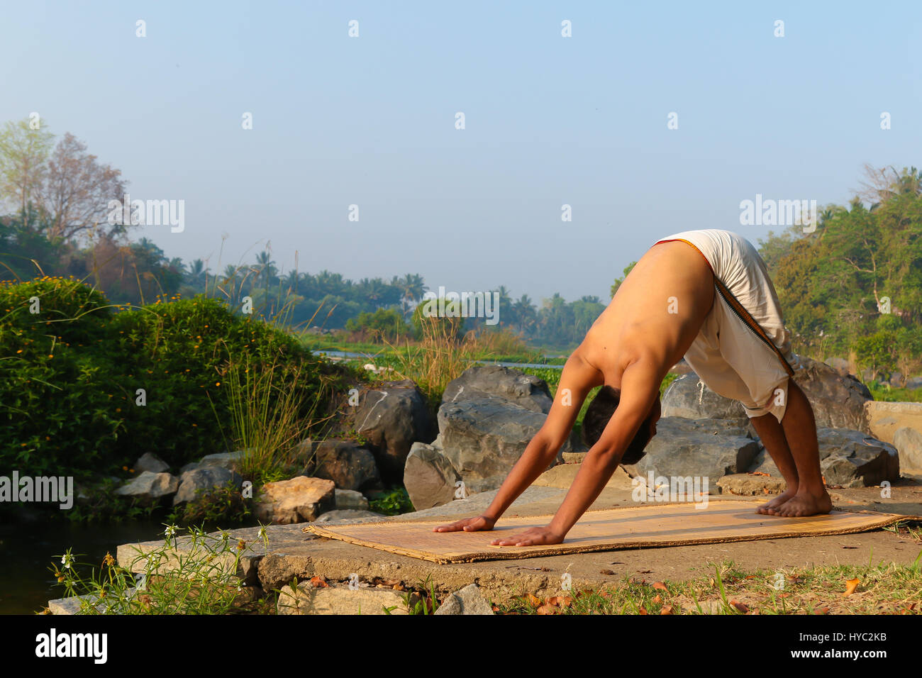 Uomo indiano a praticare yoga accanto a un fiume in India del Sud. Foto Stock