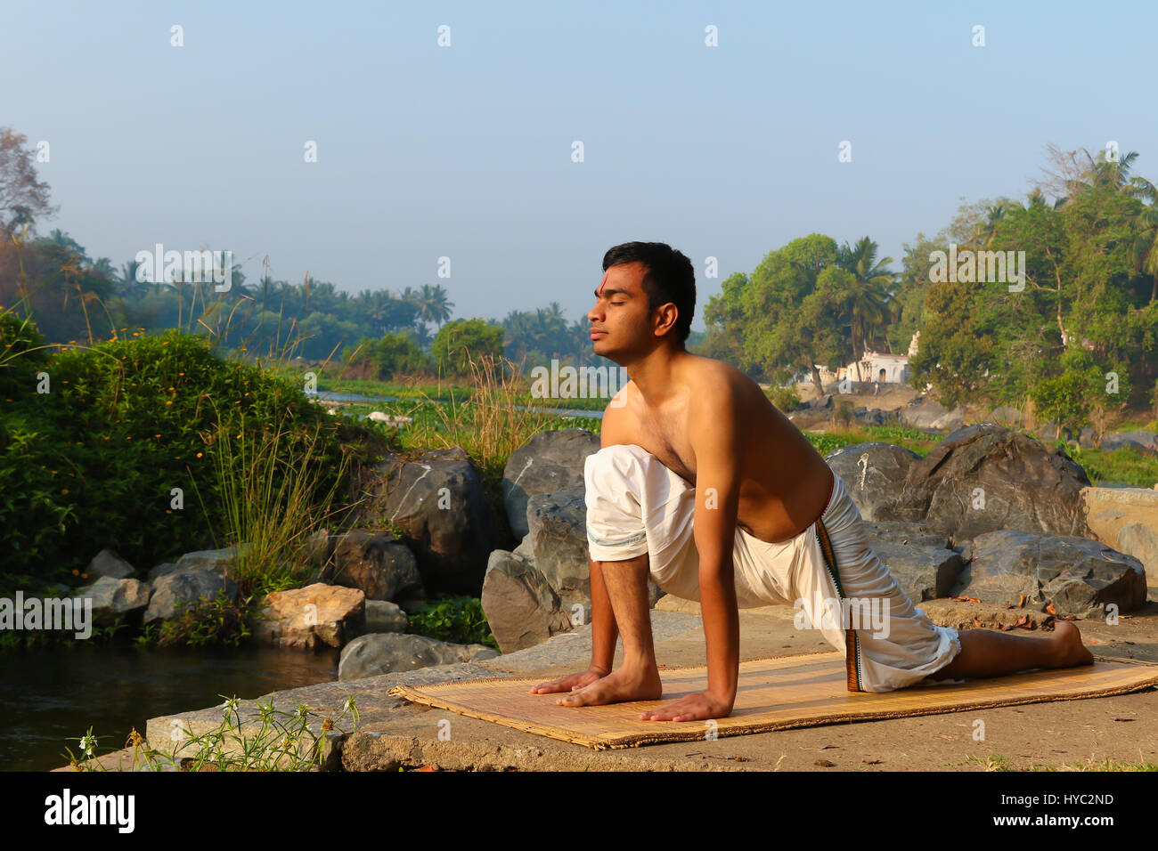 Uomo indiano a praticare yoga accanto a un fiume in India del Sud. Foto Stock
