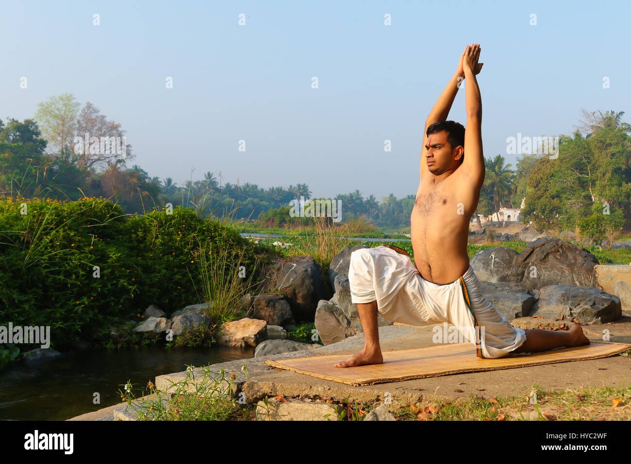 Uomo indiano a praticare yoga accanto a un fiume in India del Sud. Foto Stock