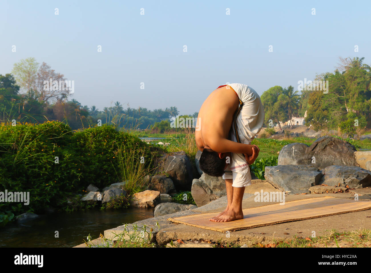 Uomo indiano a praticare yoga accanto a un fiume in India del Sud. Foto Stock