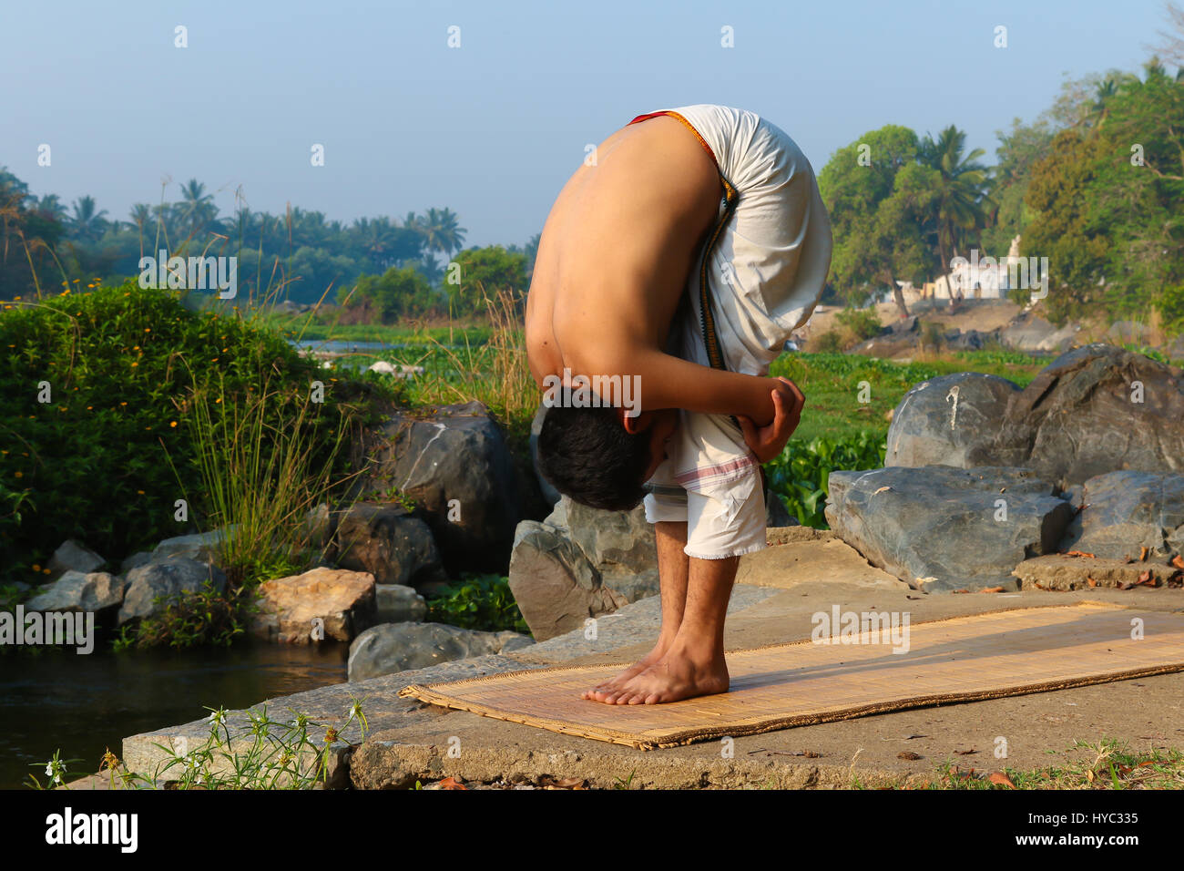 Uomo indiano a praticare yoga accanto a un fiume in India del Sud. Foto Stock