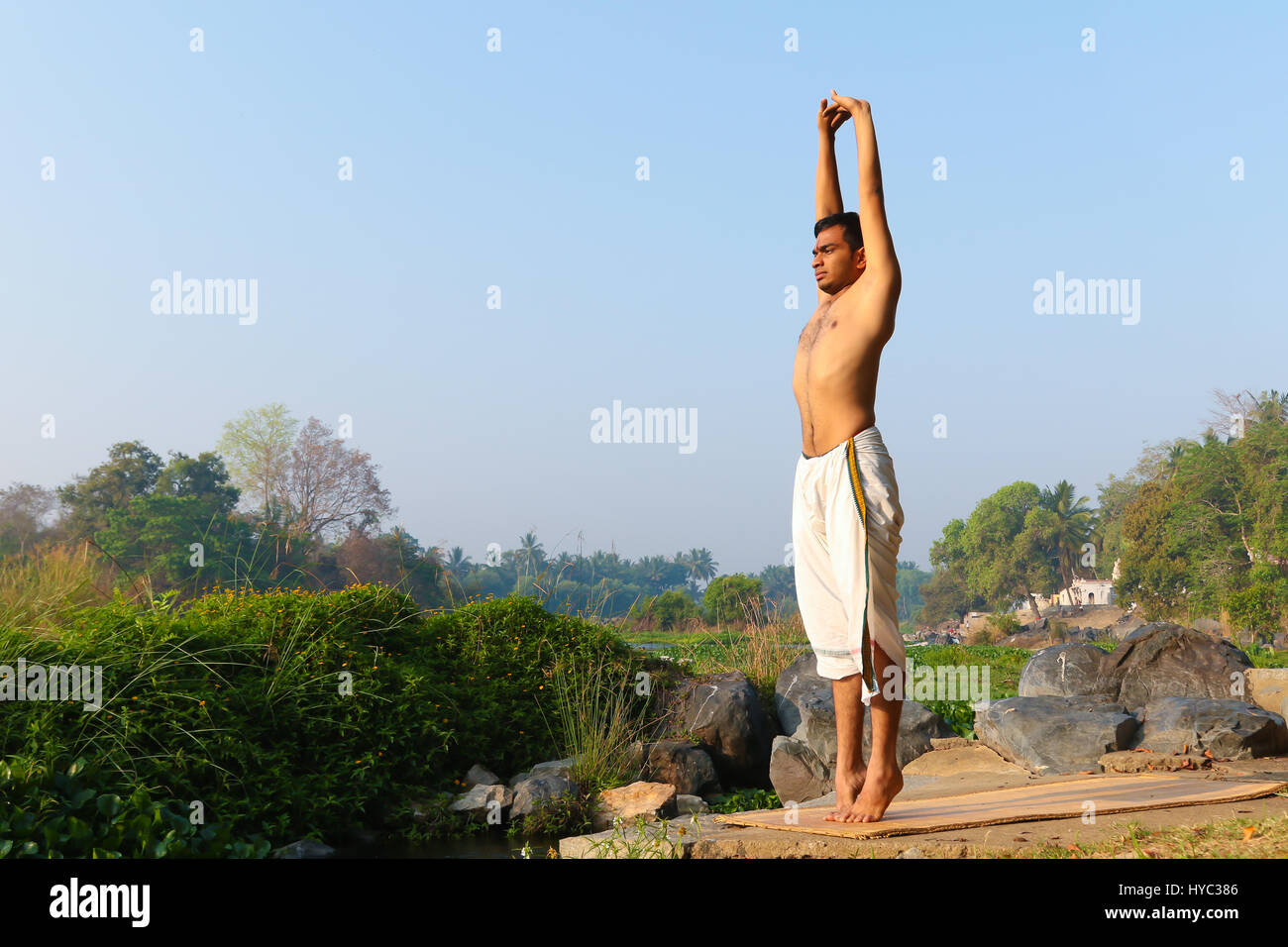 Uomo indiano a praticare yoga accanto a un fiume in India del Sud. Foto Stock