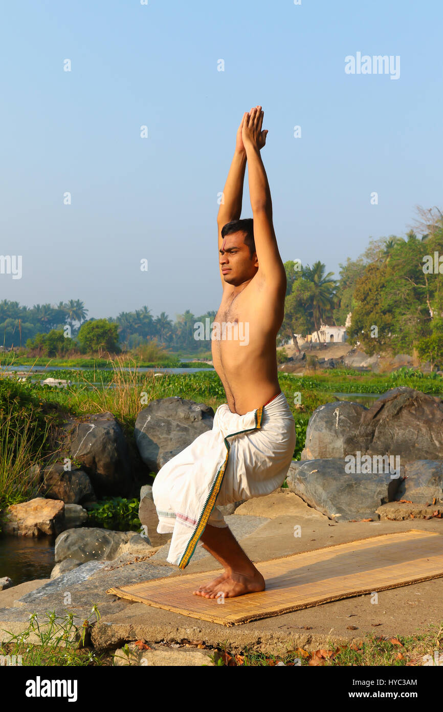 Uomo indiano a praticare yoga accanto a un fiume in India del Sud. Foto Stock