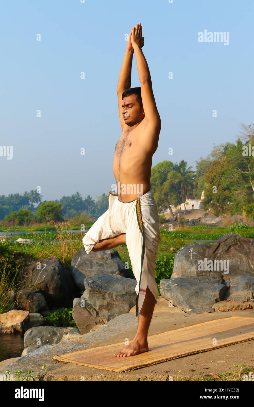 Uomo indiano a praticare yoga accanto a un fiume in India del Sud. Foto Stock