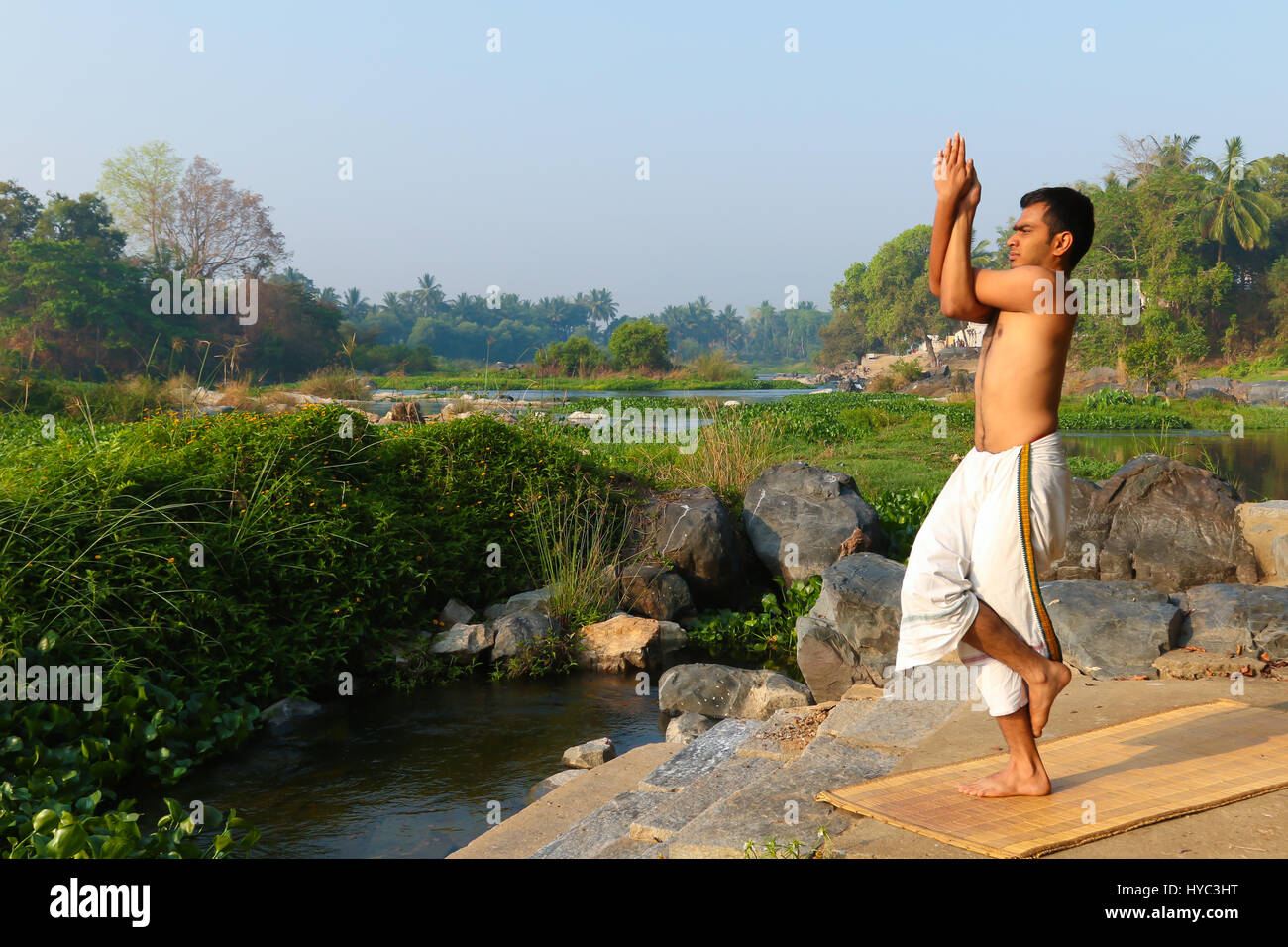 Uomo indiano a praticare yoga accanto a un fiume in India del Sud. Foto Stock