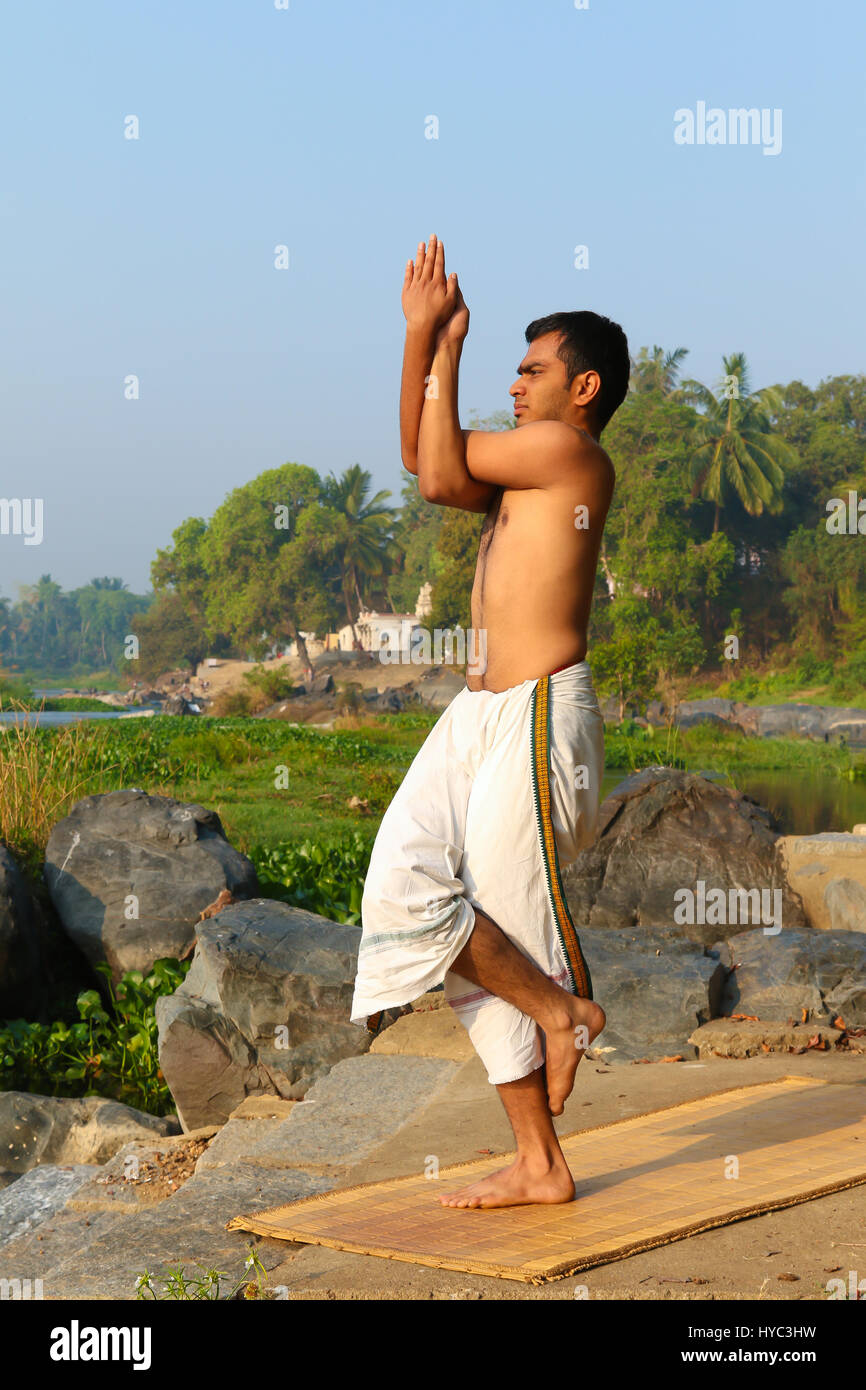 Uomo indiano a praticare yoga accanto a un fiume in India del Sud. Foto Stock