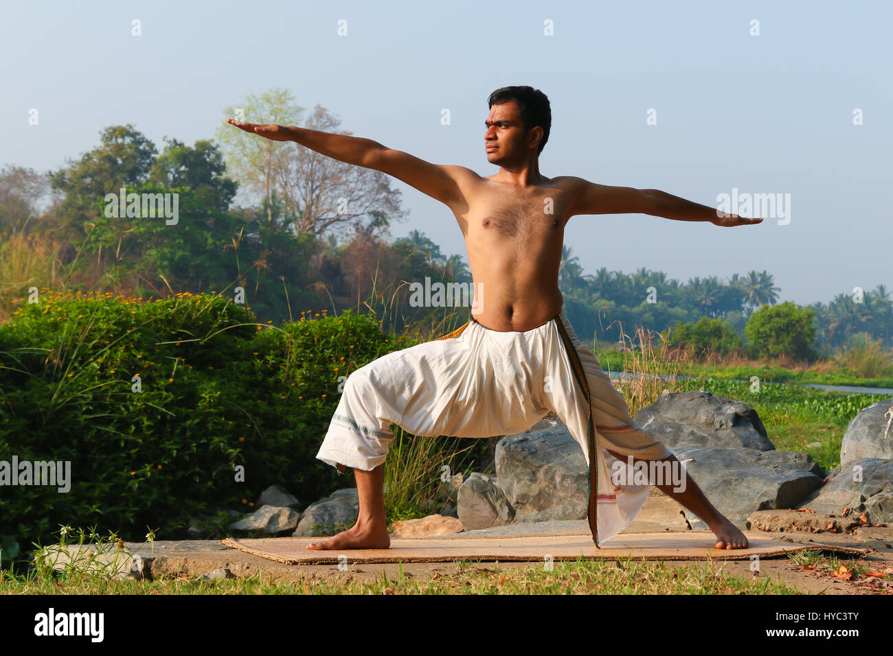 Uomo indiano a praticare yoga accanto a un fiume in India del Sud. Foto Stock