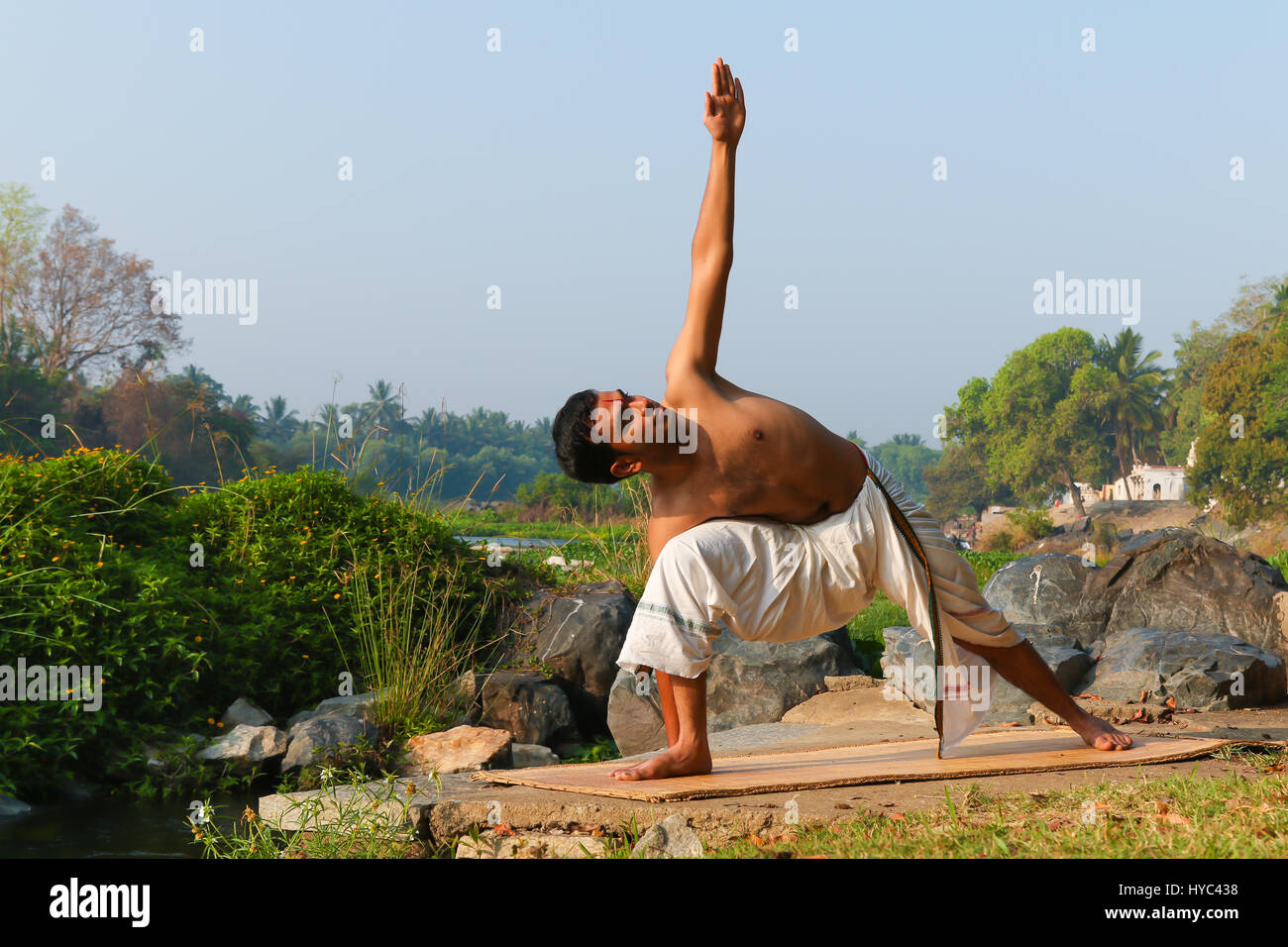 Uomo indiano a praticare yoga accanto a un fiume in India del Sud. Foto Stock