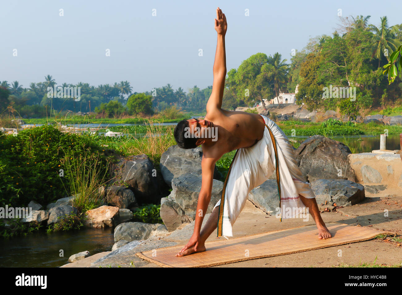 Uomo indiano a praticare yoga accanto a un fiume in India del Sud. Foto Stock