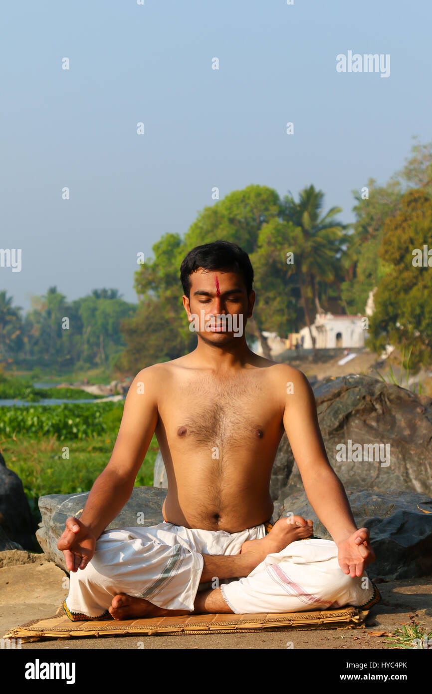 Uomo indiano a praticare yoga meditazione accanto a un fiume in India del Sud. Foto Stock