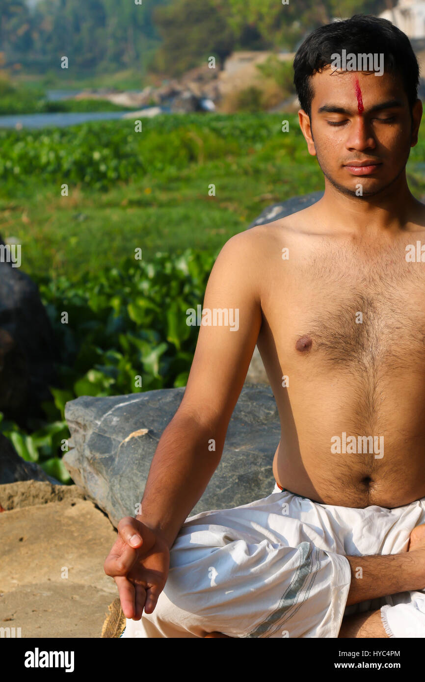 Uomo indiano a praticare yoga meditazione accanto a un fiume in India del Sud. Foto Stock