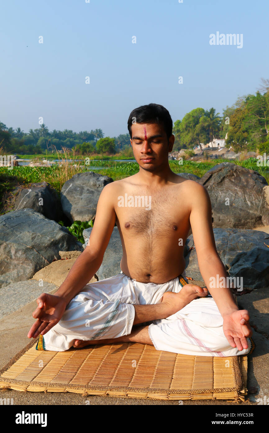 Uomo indiano a praticare yoga meditazione accanto a un fiume in India del Sud. Foto Stock