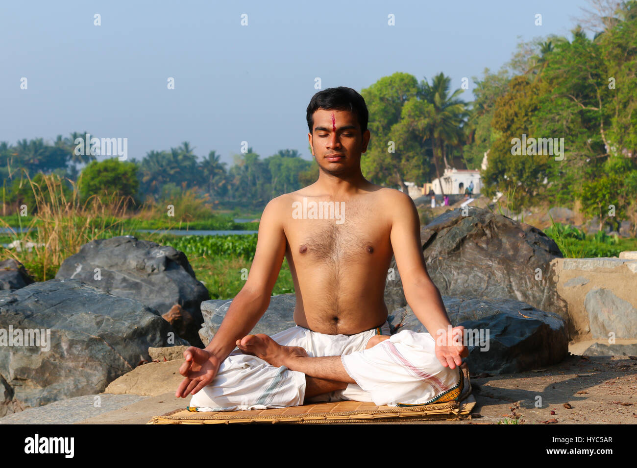 Uomo indiano a praticare yoga accanto a un fiume in India del Sud. Foto Stock