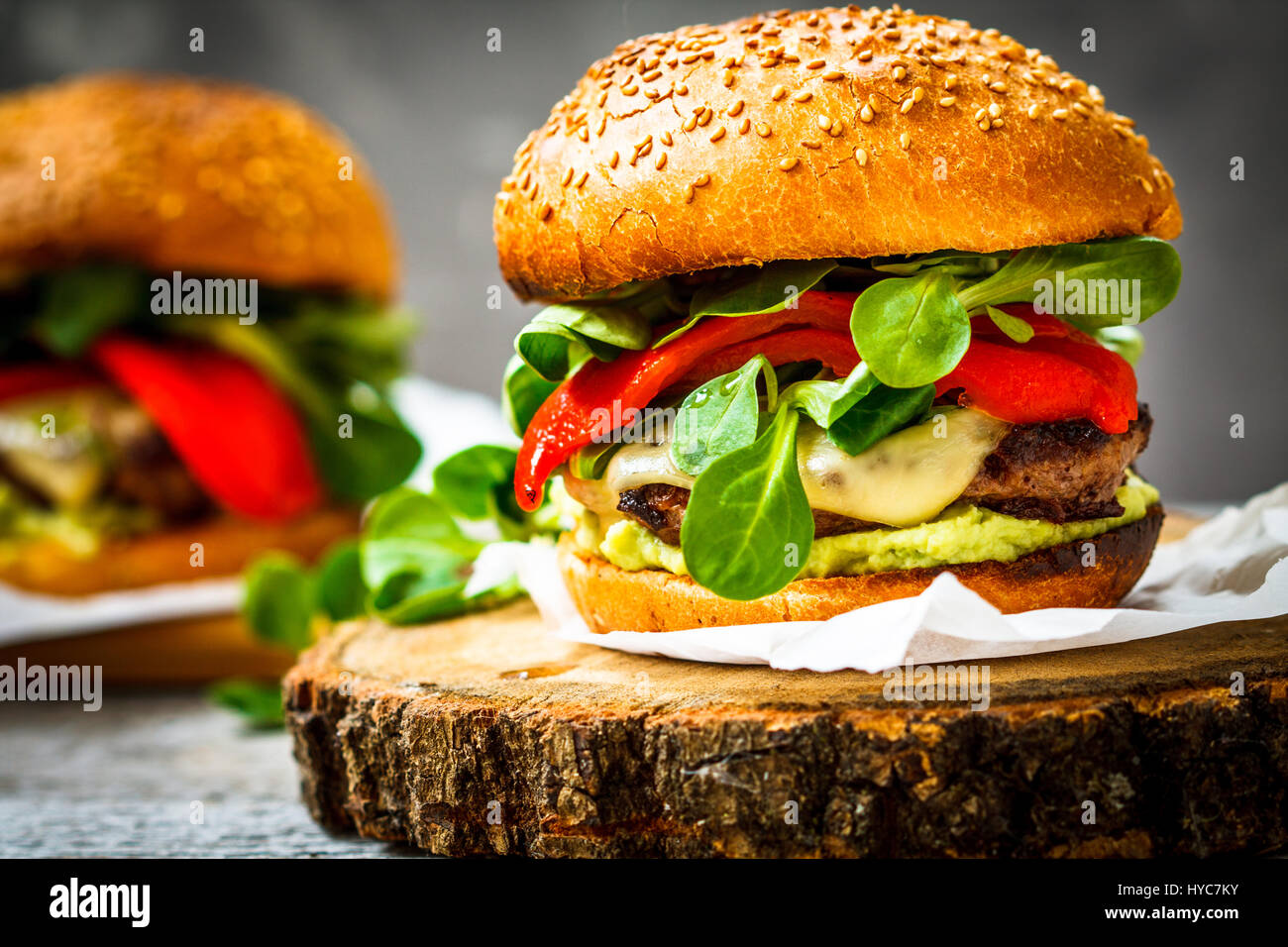 Gustosa grigliata hamburger di manzo con formaggio, guacamole e i peperoncini sott'aceto. Sfondo scuro, carta marrone, supporto di legno. Foto Stock
