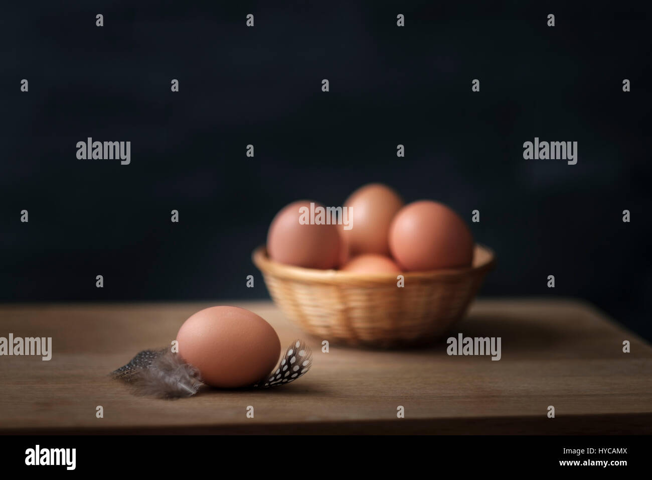 Rosolare le uova in un cesto di vimini con piume su una tavola di legno fissato contro uno sfondo nero Foto Stock