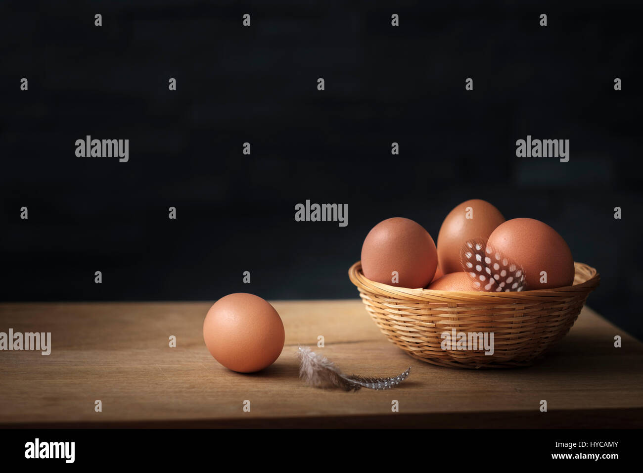 Rosolare le uova in un cesto di vimini con piume su una tavola di legno fissato contro uno sfondo nero Foto Stock
