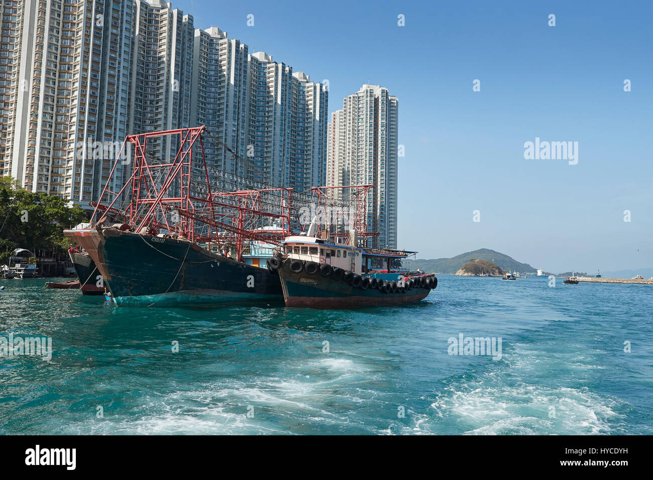 Commerciale barche da pesca ormeggiate nel canale di Aberdeen, alta edifici di appartamenti su Ap Lei Chau isola dietro. Hong Kong. Foto Stock