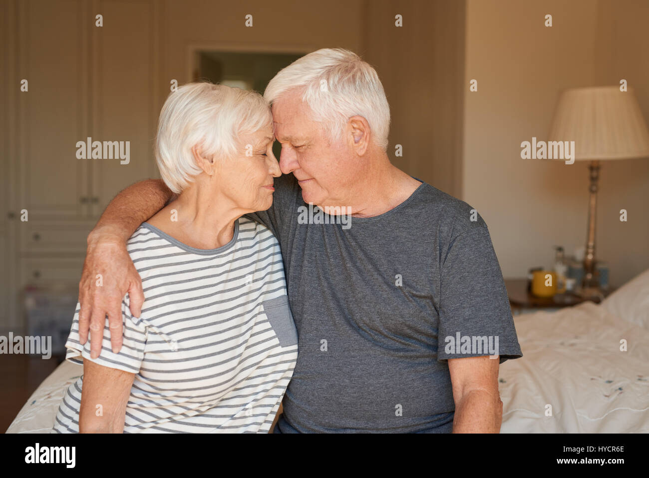 Affettuosa coppia senior seduta con gli occhi chiusi sul loro letto insieme Foto Stock