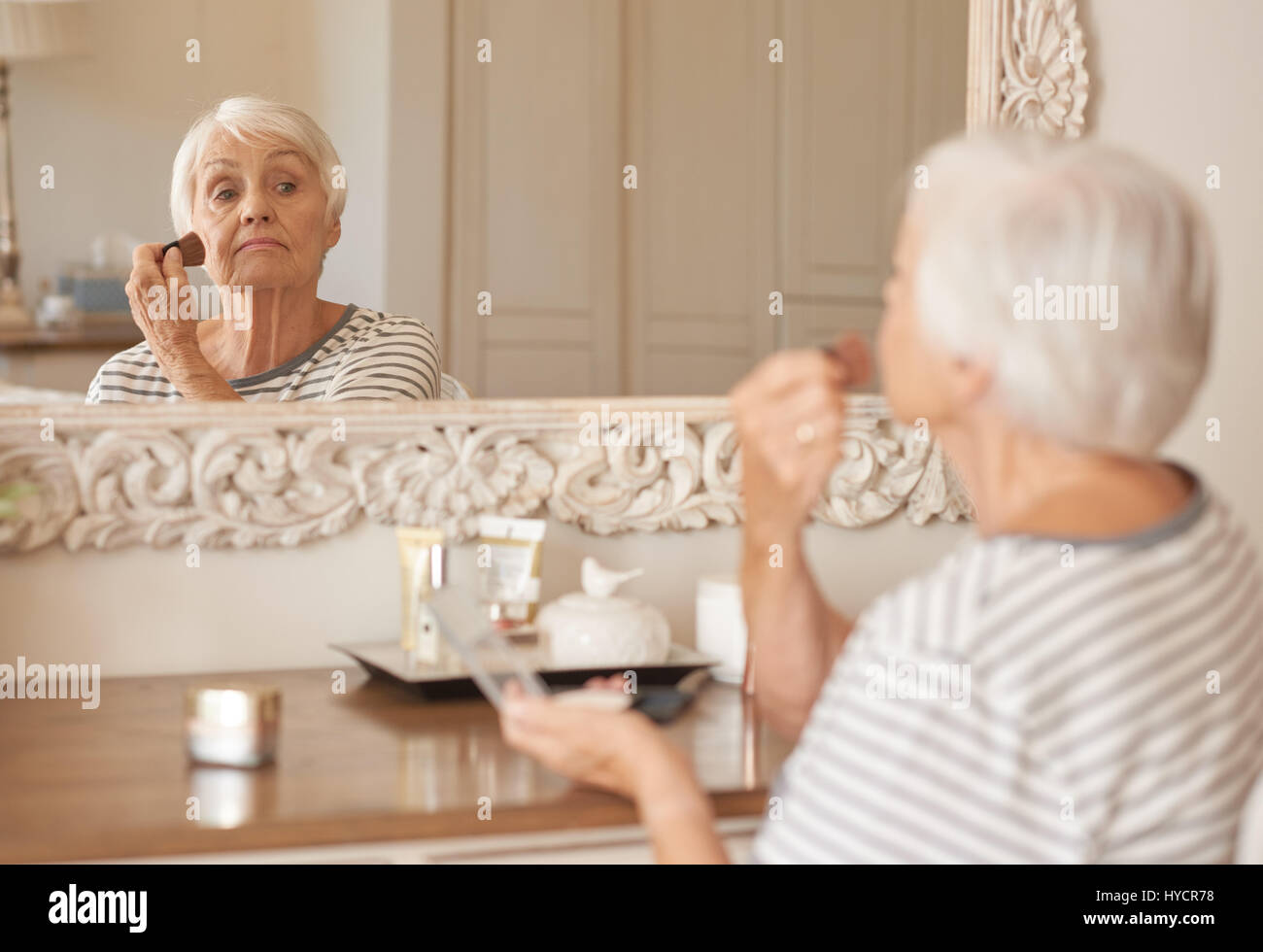 Senior donna applicare il trucco alla sua guancia in uno specchio Foto Stock