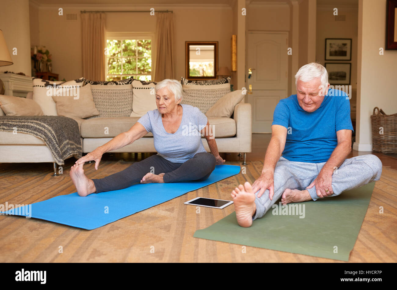 Attivo coppia senior stretching mentre fare yoga insieme a casa Foto Stock