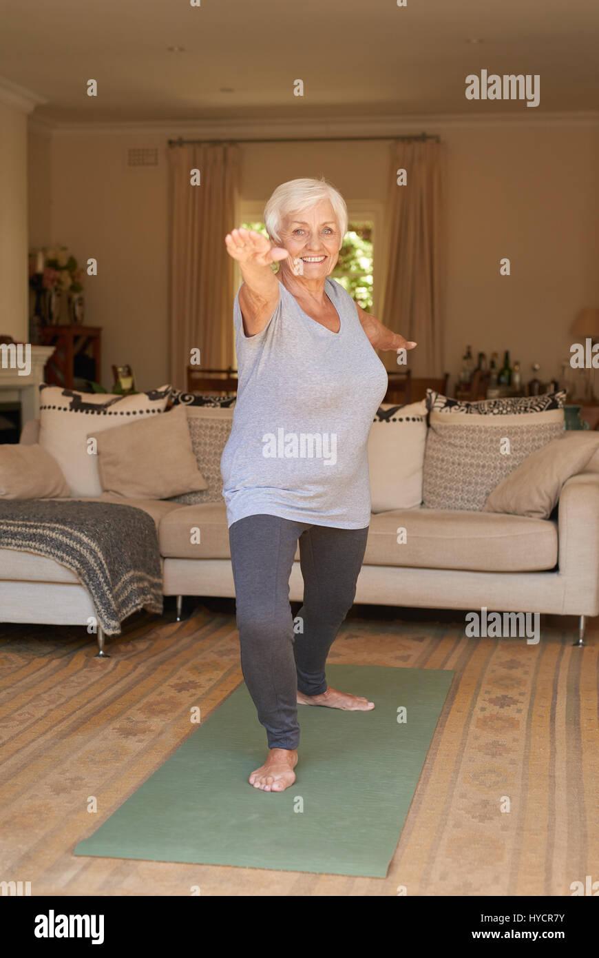 Sorridente donna senior in sportswear fare yoga a casa da solo Foto Stock