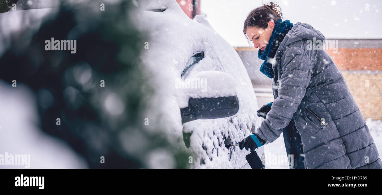 Donna che indossa grigio giacca invernale e a mano in pelle Guanti neve di sblocco auto coperto Foto Stock