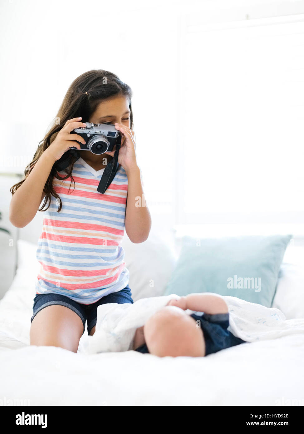 Ragazza (10-11) scattando una foto al fratello minore (12-17 mesi) sdraiato sul letto Foto Stock