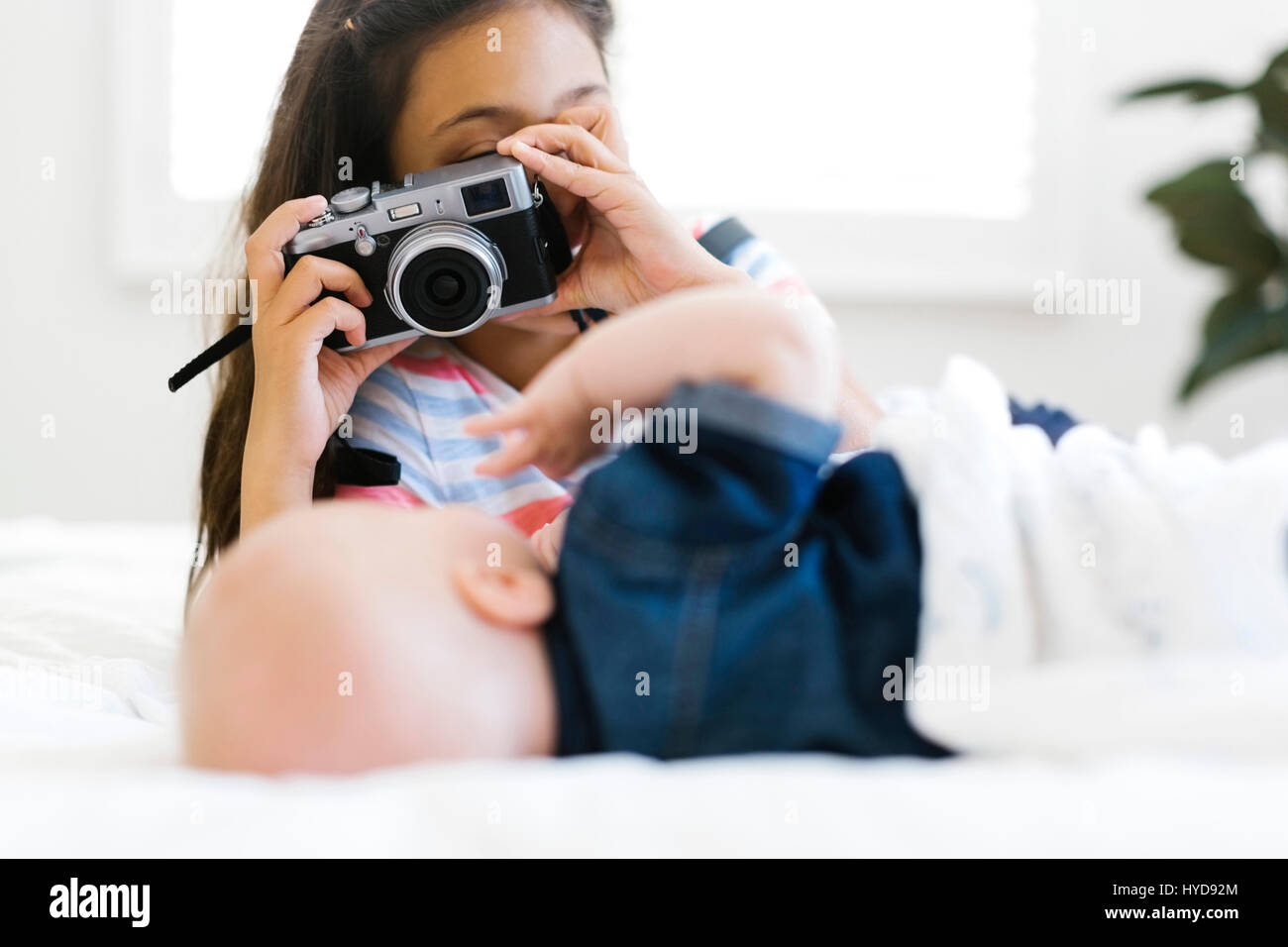Ragazza (10-11) scattando una foto al fratello minore (12-17 mesi) sdraiato sul letto Foto Stock
