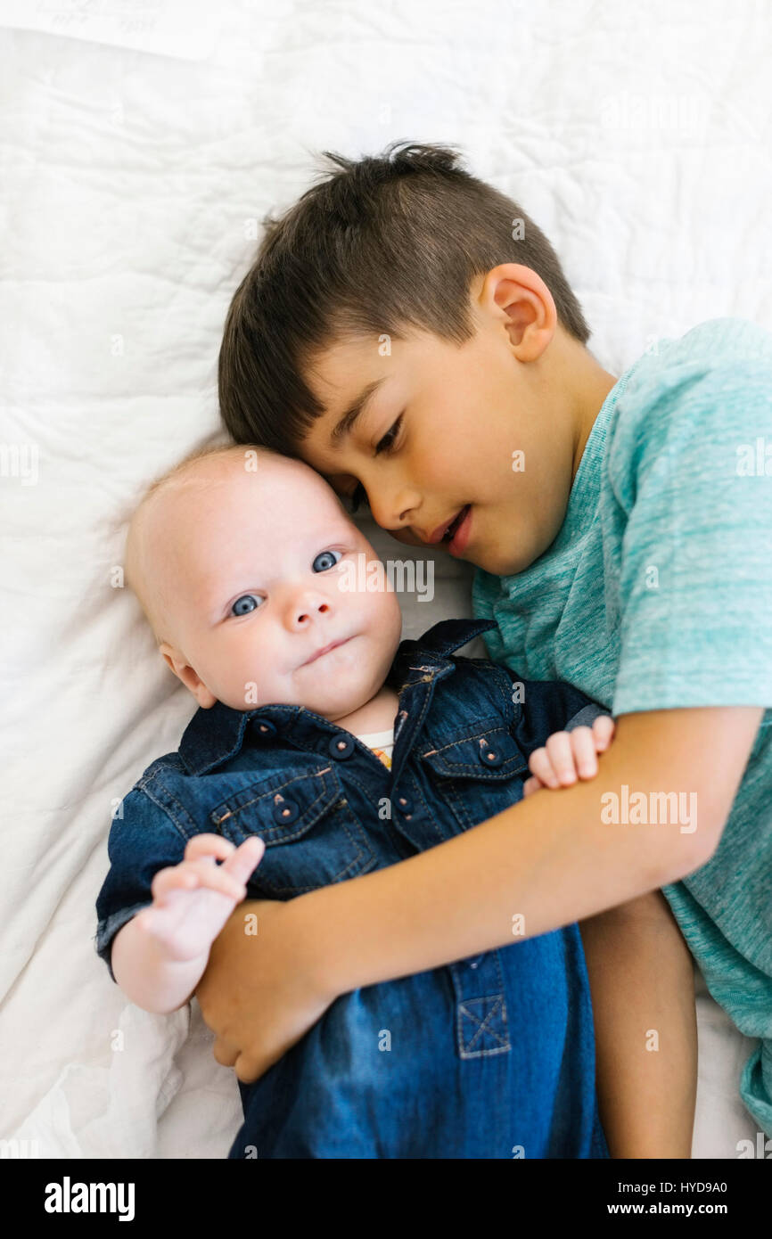 Due fratelli (6-11 mesi) sdraiati a letto e abbracciati Foto Stock