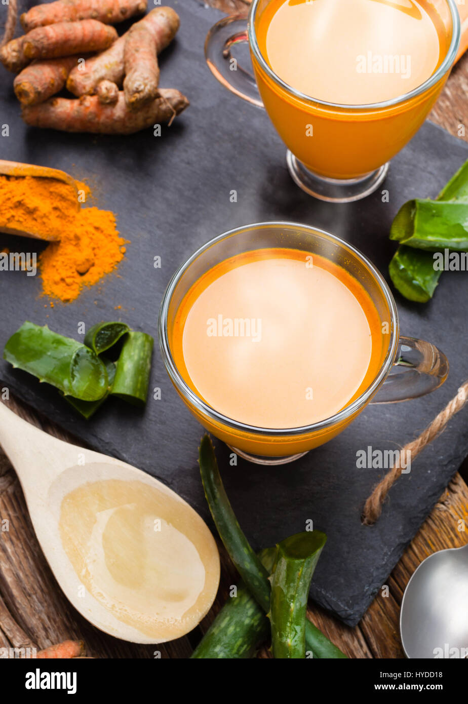 Bevanda calda con aloe vera e la curcuma. Le coppe di vetro su un vassoio di ardesia Foto Stock