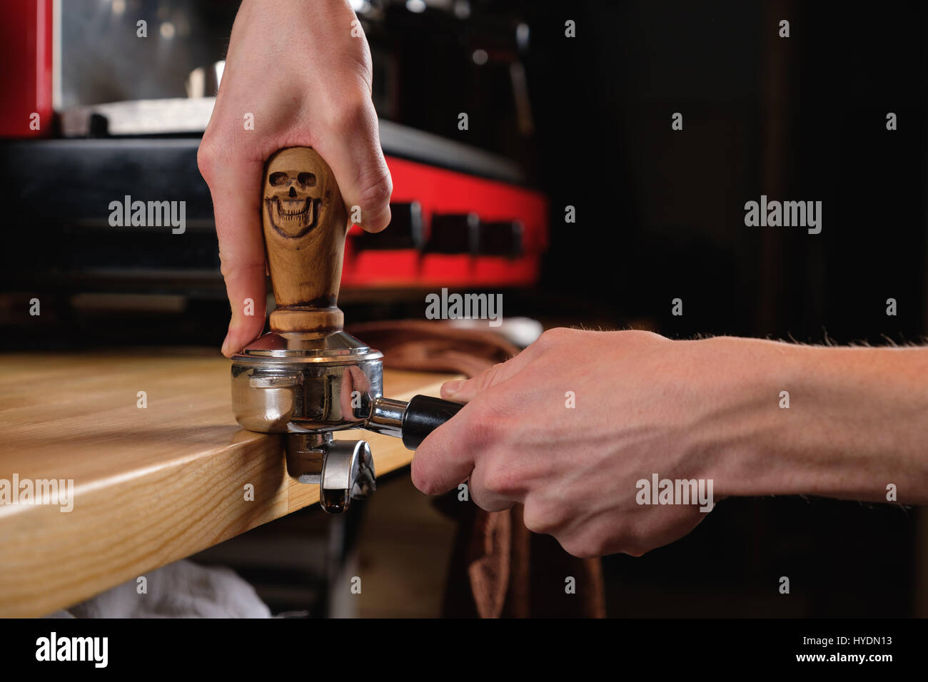 Barista utilizzando una tempera con manico in legno per premere il caffè appena macinato in una compressa Foto Stock