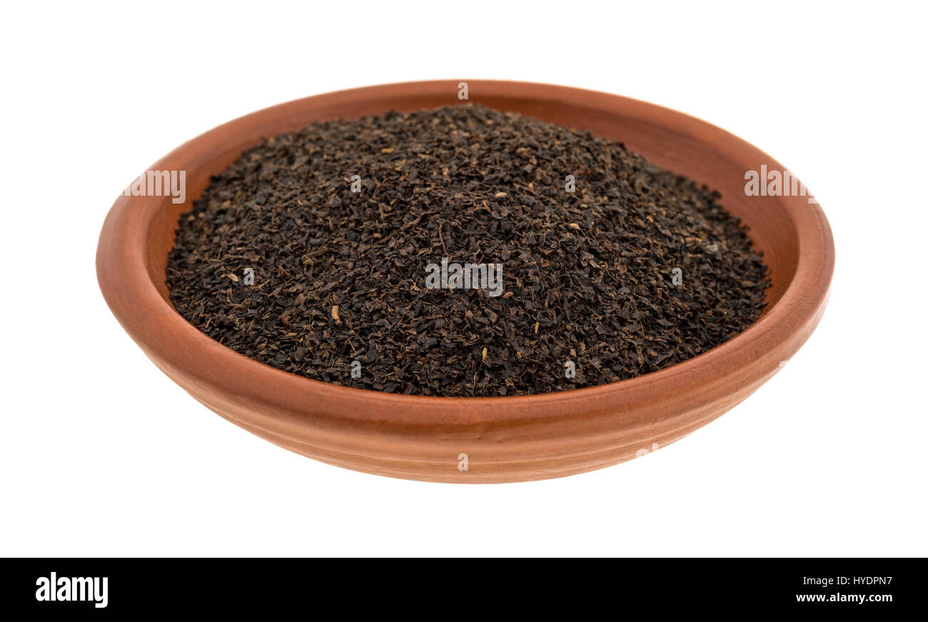Una piccola ciotola di argilla riempita con sciolto foglie di tè nero isolato su uno sfondo bianco. Foto Stock