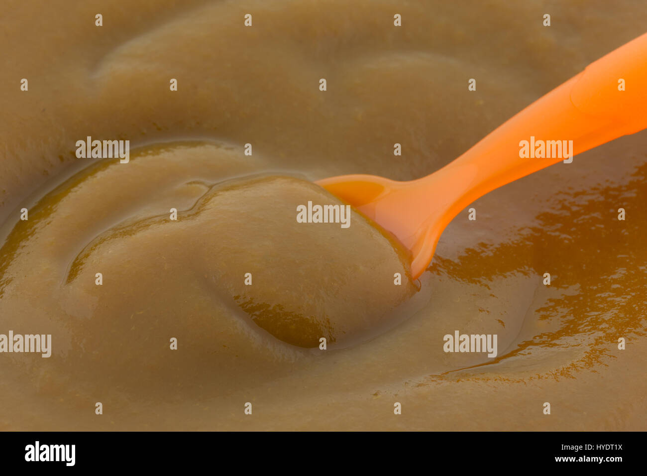 Vista ravvicinata di Apple e di sfrondare la purea di pappe per bambini con un'arancia cucchiaio di plastica. Foto Stock