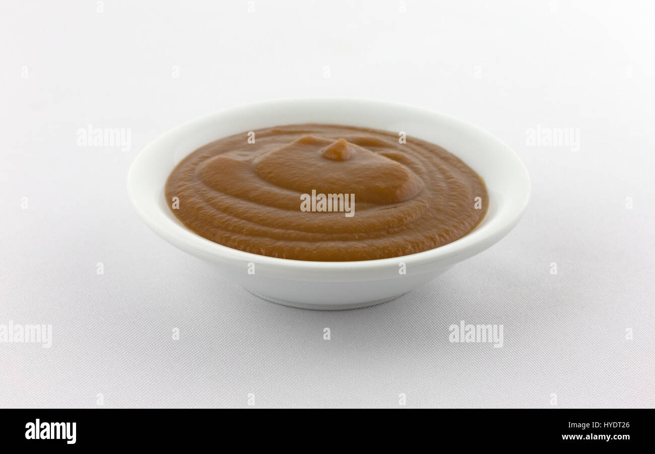 Vista laterale di una piccola ciotola riempita con Apple e potare la purea di pappe per bambini sulla cima di una tovaglia bianca. Foto Stock