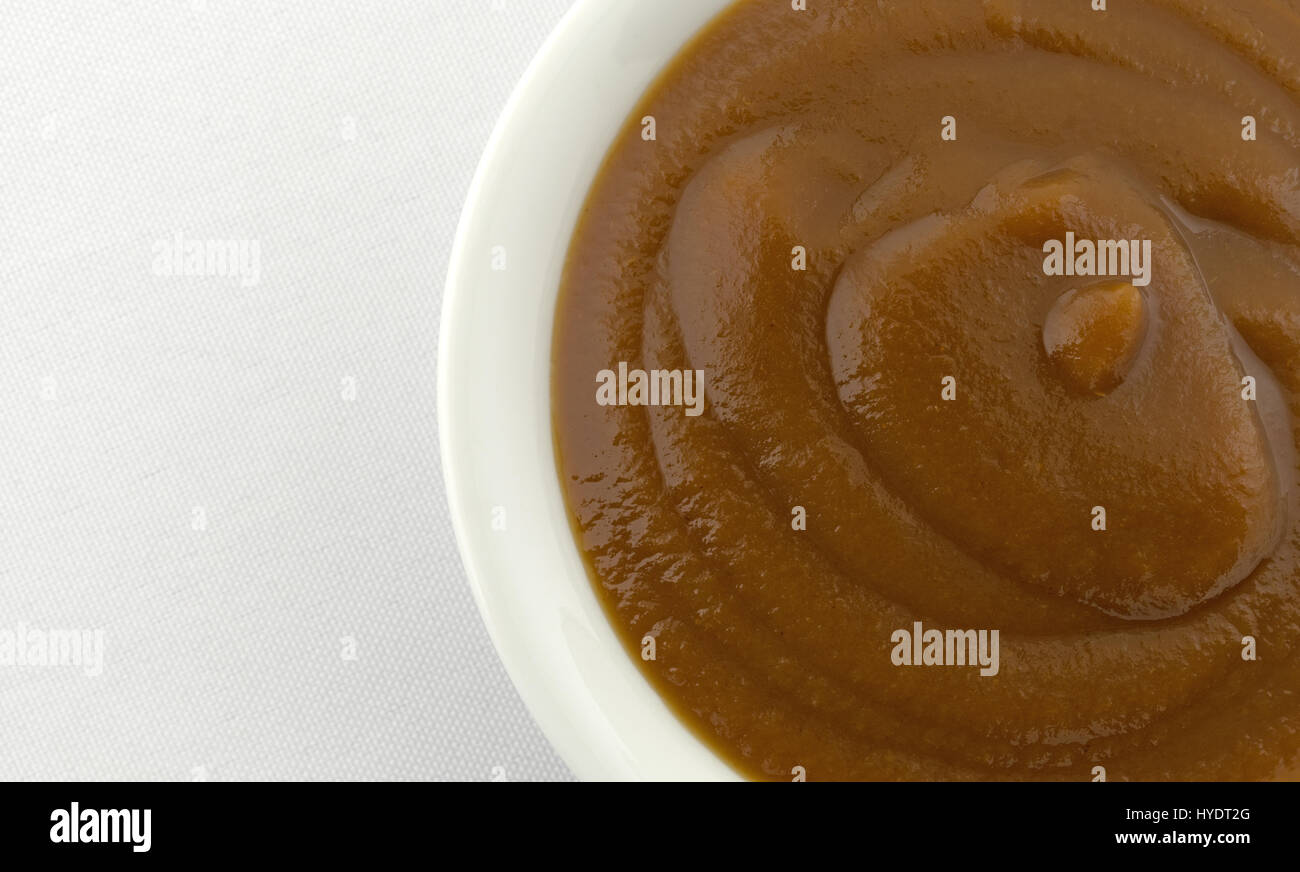 Top vista ravvicinata di una piccola ciotola riempita con Apple e potare la purea di pappe per bambini sulla cima di una tovaglia bianca. Foto Stock