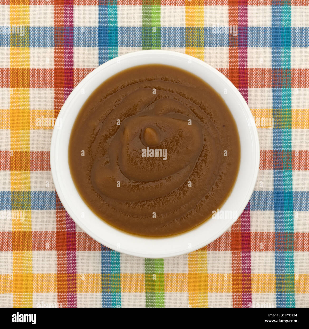 Vista dall'alto di una piccola ciotola bianco riempito con Apple e potare la purea di cibo per neonati in cima a una tovaglia colorata. Foto Stock