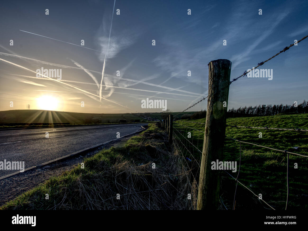 Tramonto sulla strada di campagna,jet tracce su sky nel Parco Nazionale di Peak District,Derbyshire, Regno Unito. Foto Stock