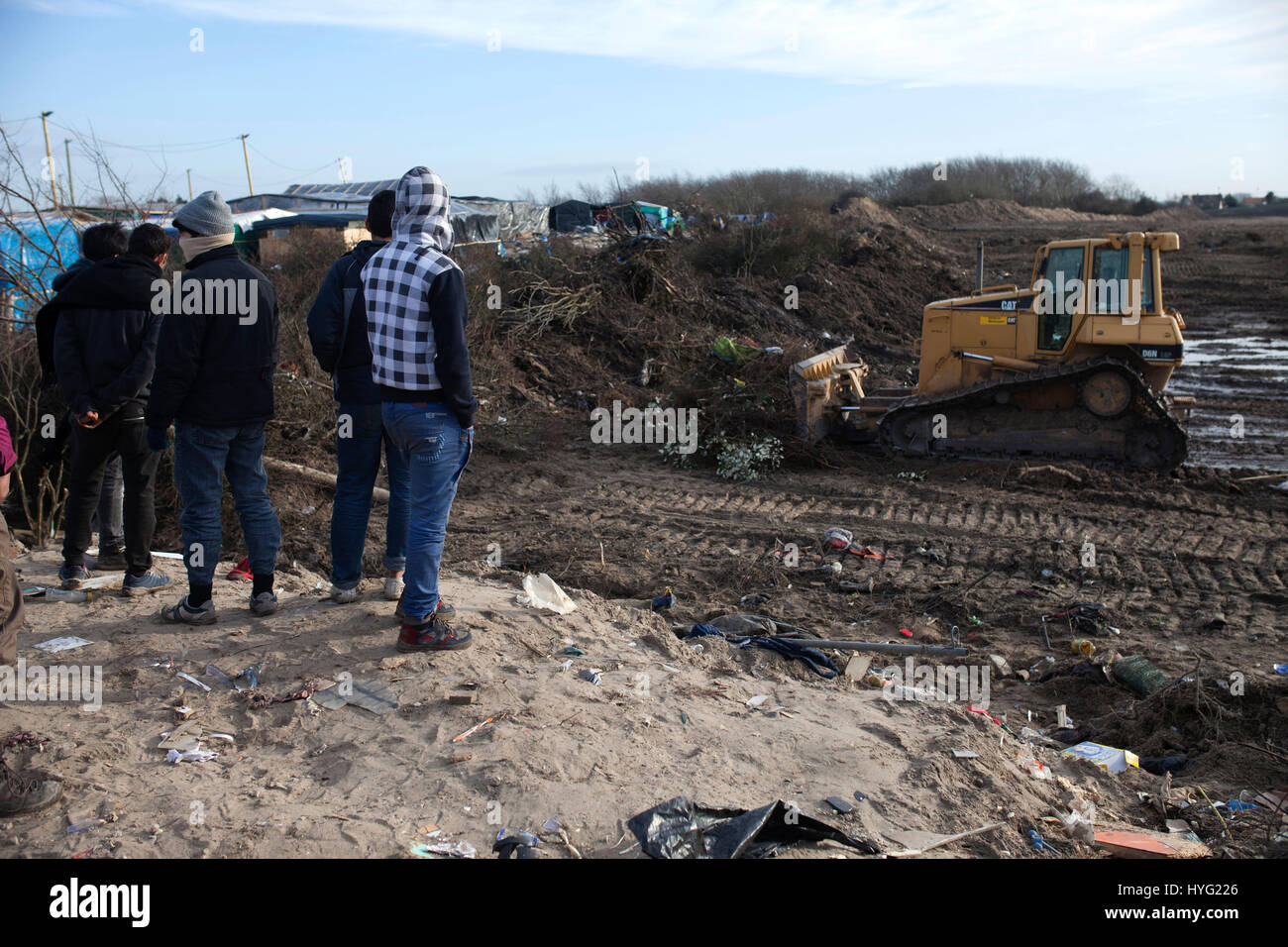 Gennaio,2016. I rifugiati guarda la demolizione di un area dove i rifugiati avevano costruito rifugi in campo profughi nelle dune di Calais, Francia.Il campo di rifugiati a Calais è nelle fasi finali di essere cancellato dalla polizia francese. Le immagini mostrano come bulldozer protetti da agenti di sicurezza hanno lasciato quasi una traccia di ciò che una volta erano strettamente impaccate rifugi. Il controverso camp, che è stata la casa di circa 6.000 migranti principalmente dalla Siria e dal Nord Africa, viene rimosso in maniera costante da parte delle autorità. Foto Stock