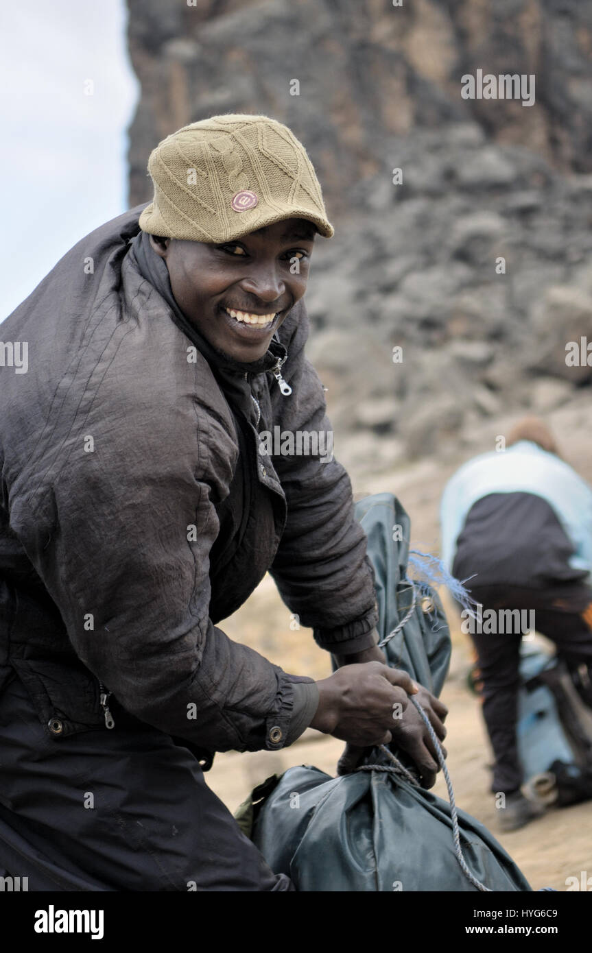 Uomo sorridente mentre il suo imballaggio borsa alla torre di Lava Camp, il Monte Kilimanjaro National Park, Tanzania Foto Stock