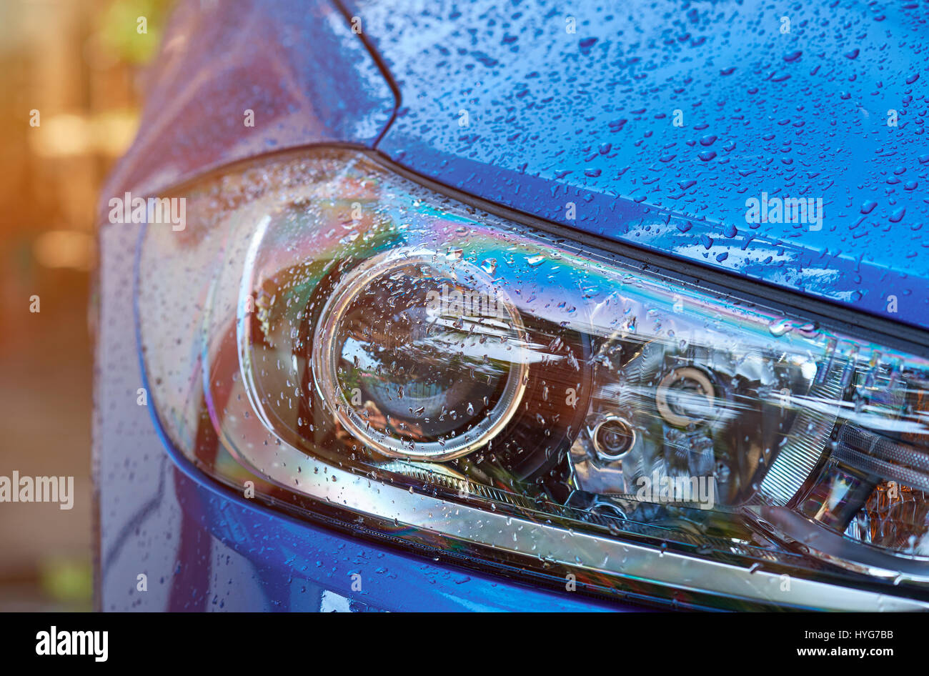 Wet Blue faro auto close-up. Auto di lusso luce di testa in gocce di pioggia acqua Foto Stock
