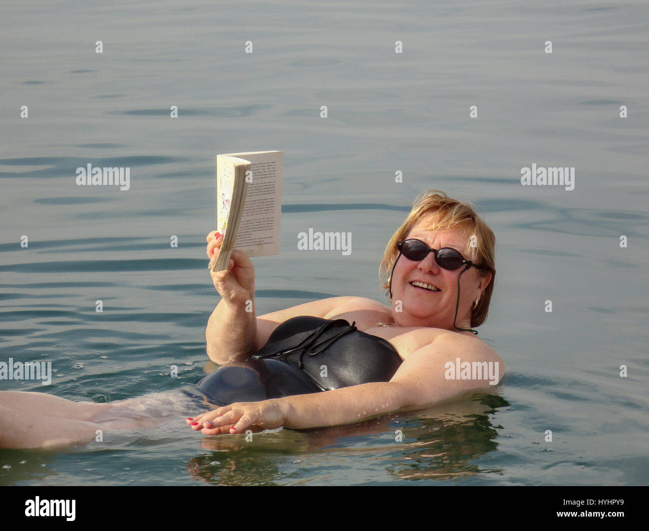 Una donna galleggianti in te Mar Morto la lettura di un libro tascabile. Foto Stock