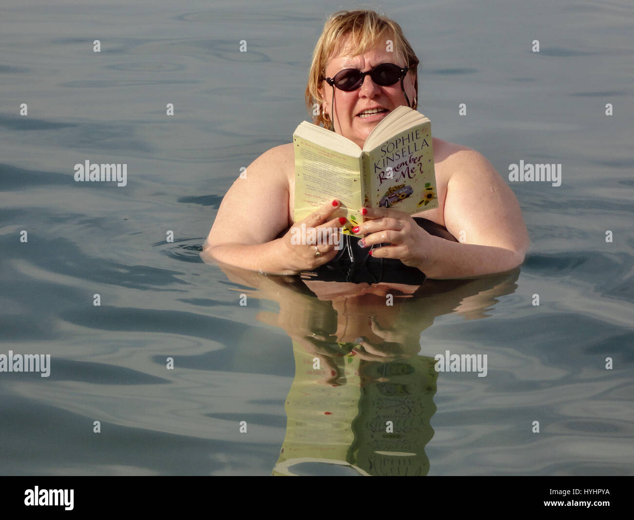 Una donna galleggianti in te Mar Morto la lettura di un libro tascabile. Foto Stock
