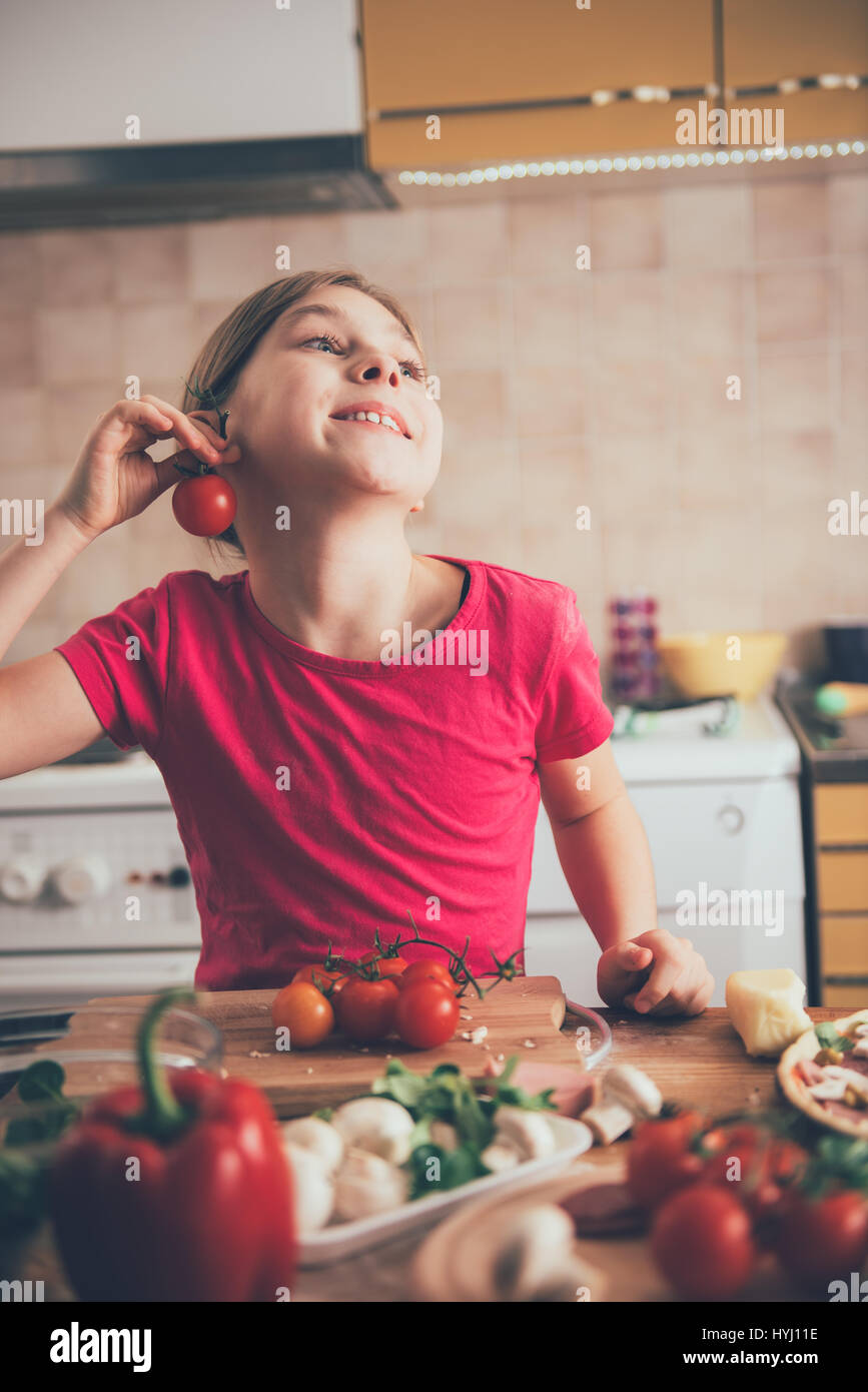 Carino bambina ingannare intorno con il pomodoro in cucina Foto Stock