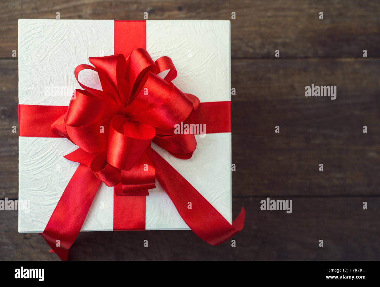 Confezione regalo con fiocco rosso sulla tavola di legno, vista dall'alto Foto Stock