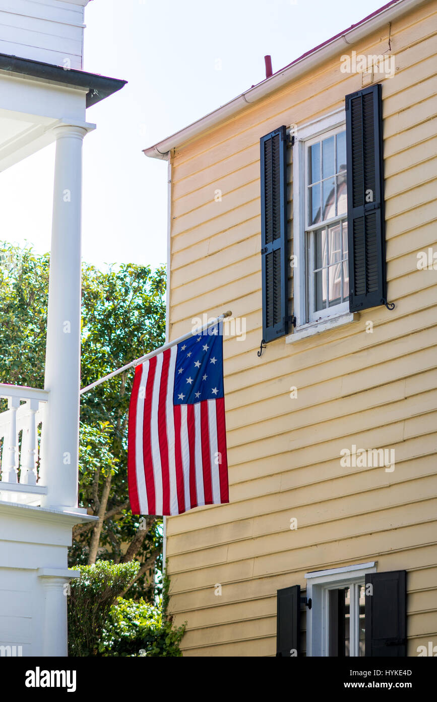 Una storica bandiera americana pende off coloniale bianco portico adiacente ad una casa gialla a Charleston, Carolina del Sud durante i mesi estivi. Foto Stock