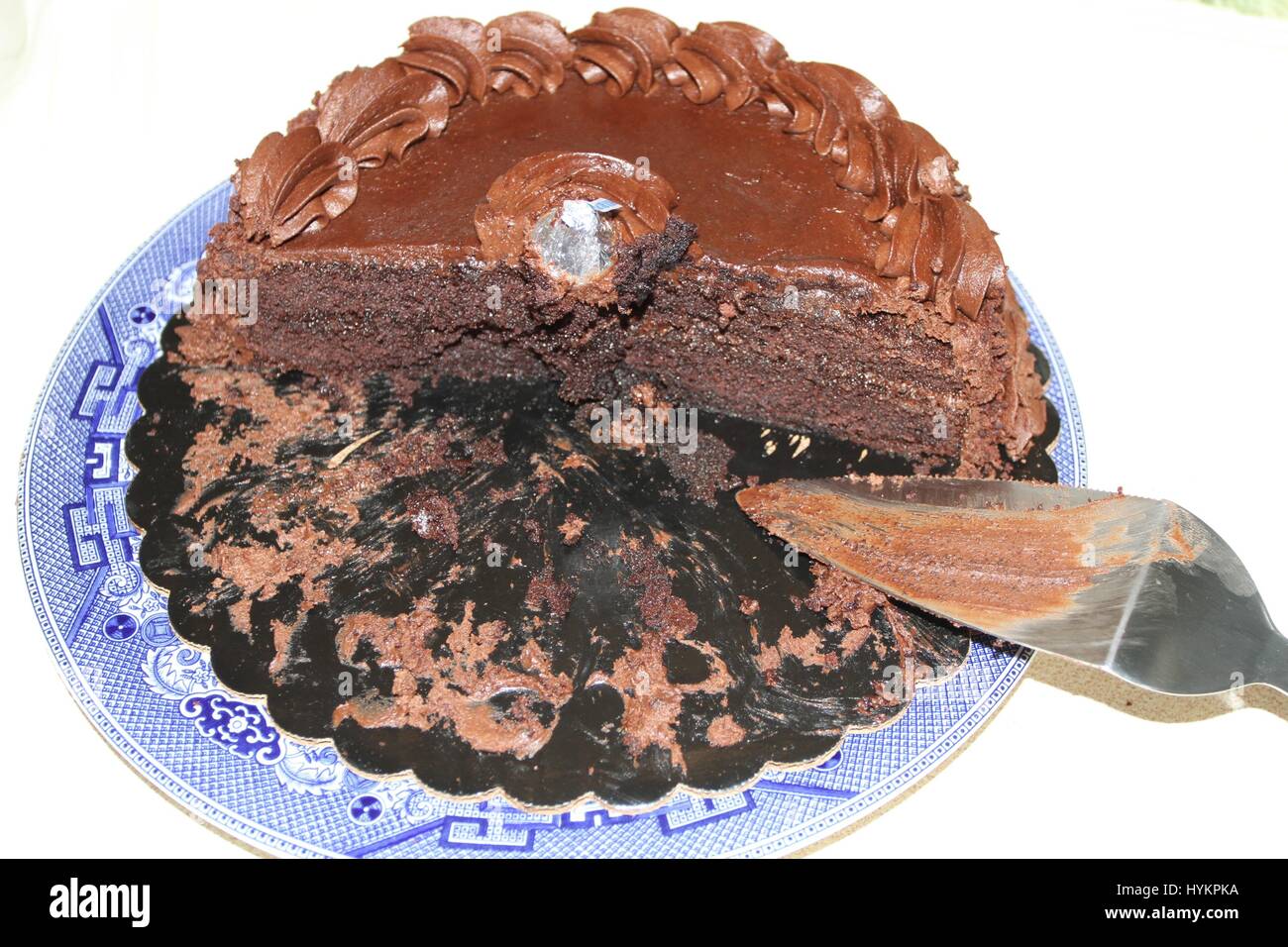 Un round dolce torta al cioccolato con crema di colore marrone su un grande blu e bianca porcellana piatto. La metà della torta e Server la torta su un piatto da portata. Torta di vacanza. Foto Stock